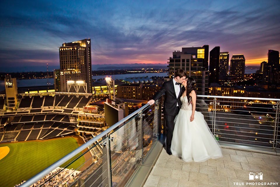 newly married couple kissing on the terrace of diamond view tower with the san diego skyline and sunset in the background