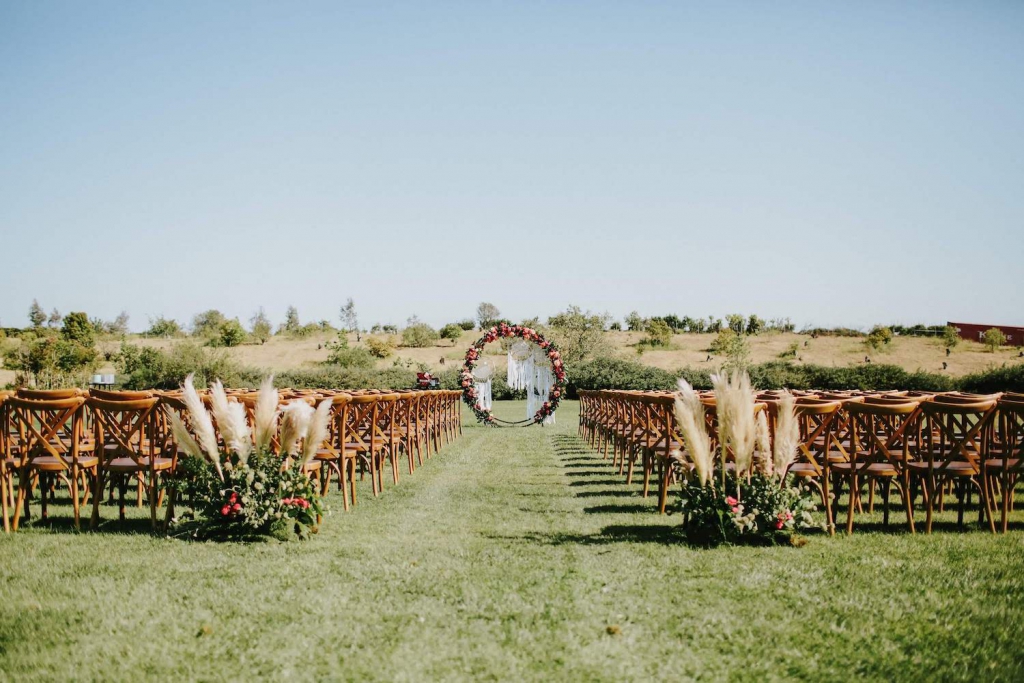 a circular wedding arch covered in flowers, and chairs set up for a wedding, on a grassy field