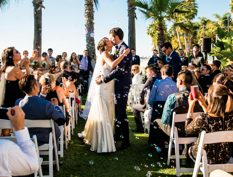 bride and groom kiss as they walk down the aisle at wedding ceremony in paradise point in san diego