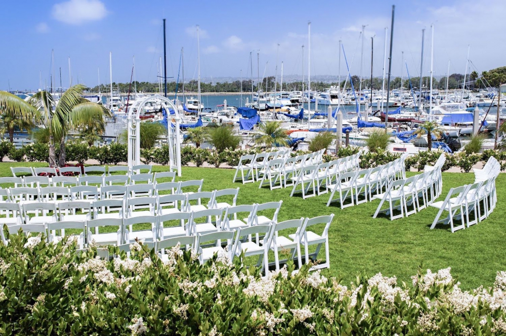 white chairs set up for a wedding on a green lawn overlooking the marina at the dana on mission bay