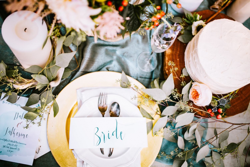 table setting at winter wedding reception with a blue table cloth, and white candles, red berries, and eucalyptus sprigs on the table