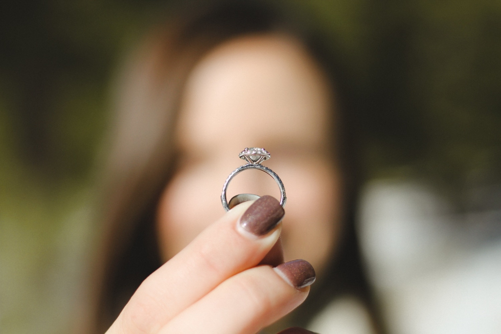 woman out of focus holding up engagement ring