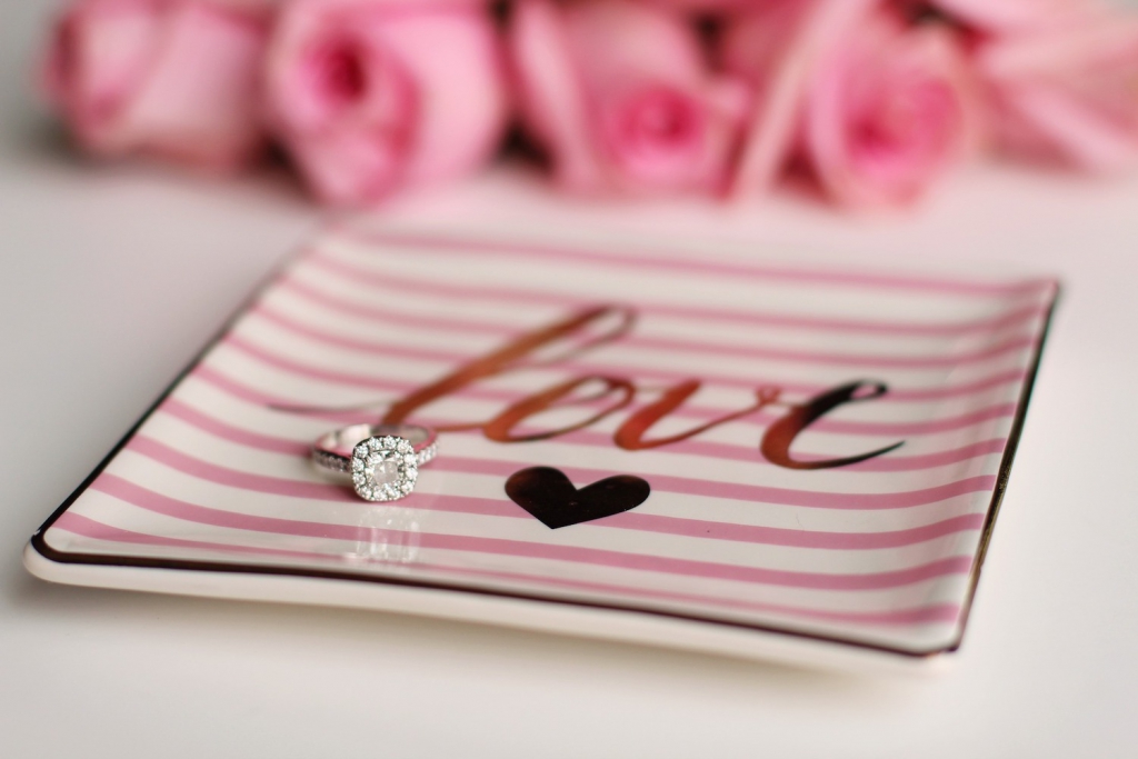 sparkly engagement ring sitting on a pink-striped plate that says love