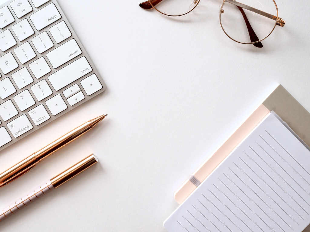 Apple keyboard with glasses, notepad, and pens