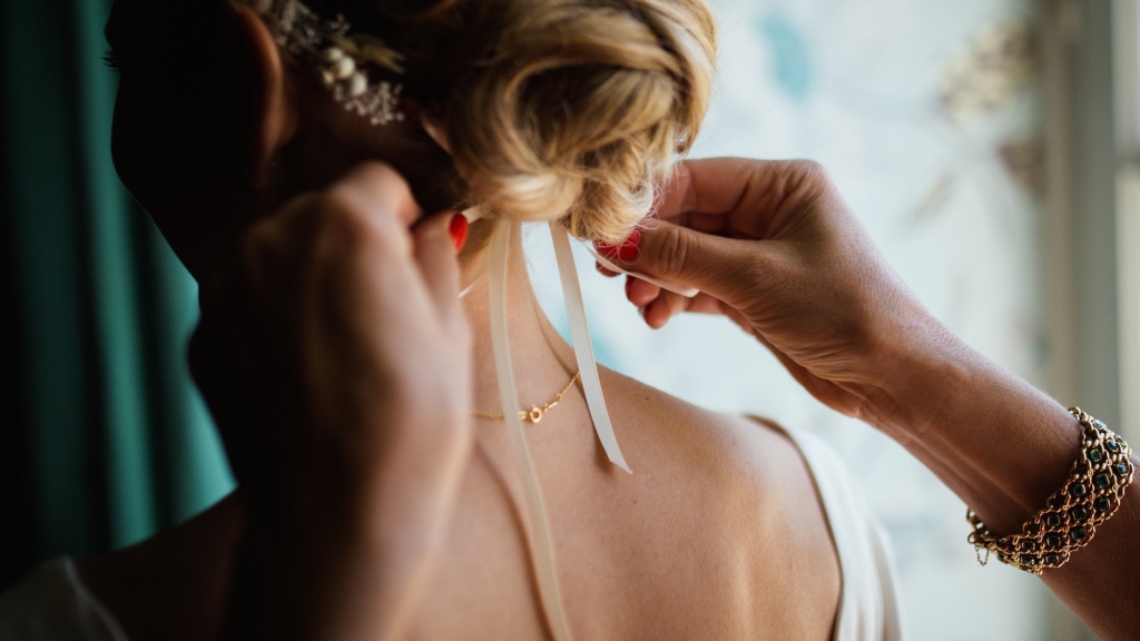 woman tying a white ribbon around bride's hair